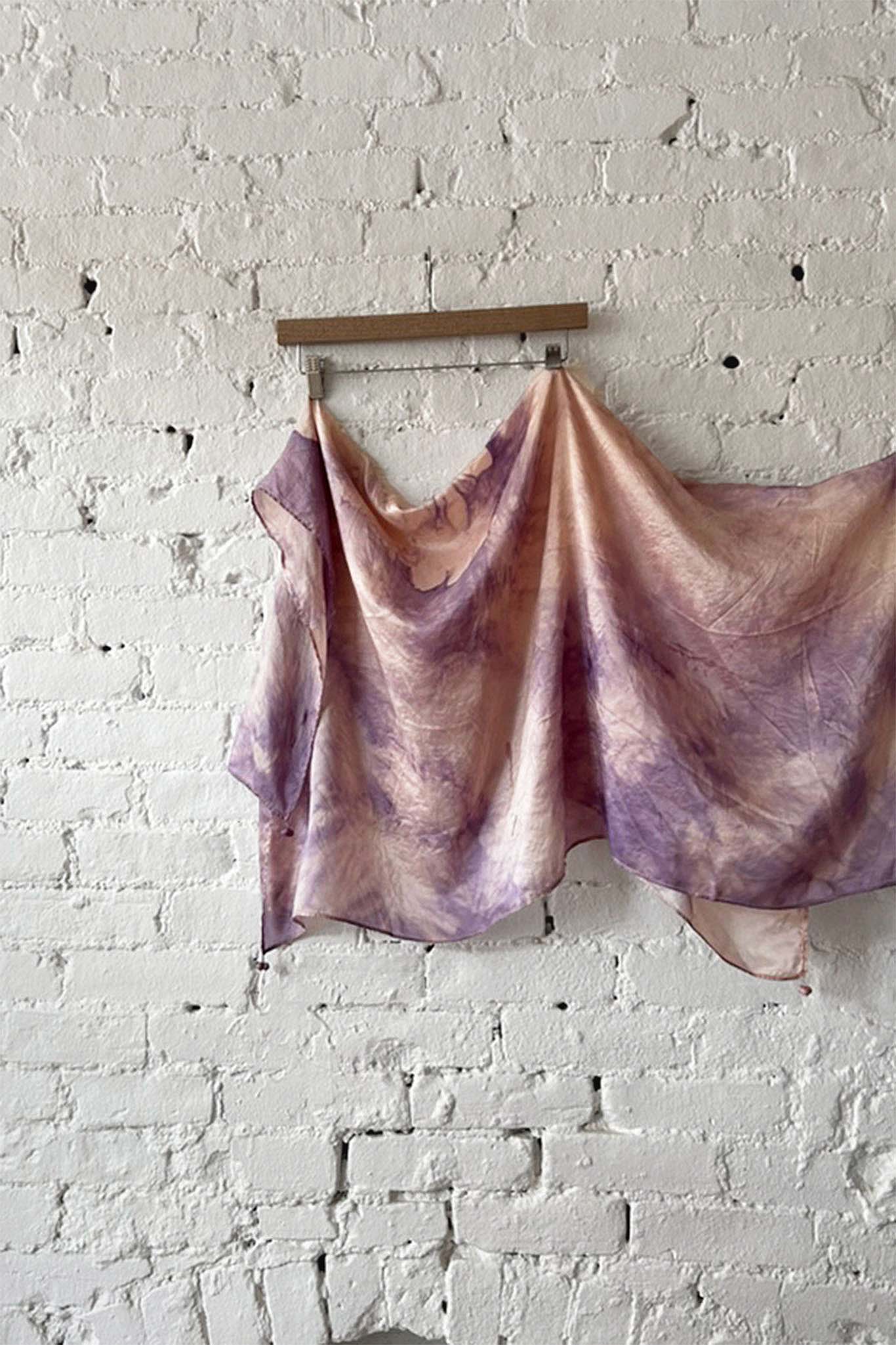Purple and pink tie-dye silk scarf hanging against a white brick wall