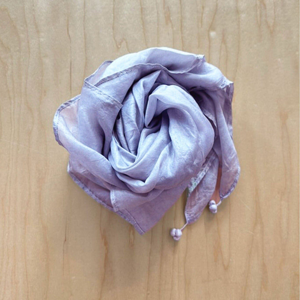 Folded light purple silk scarf with tassel accents on a wooden surface