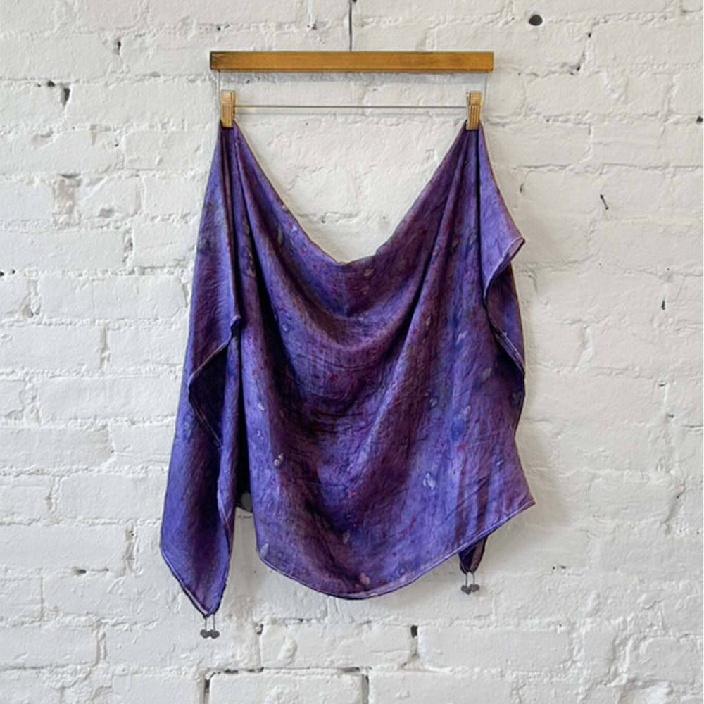 Purple silk scarf draped over a wooden hanger against a white brick wall.