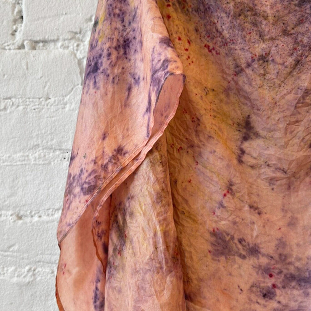 Tie dye silk scarf with earthy tones draped over a surface against a white brick wall.