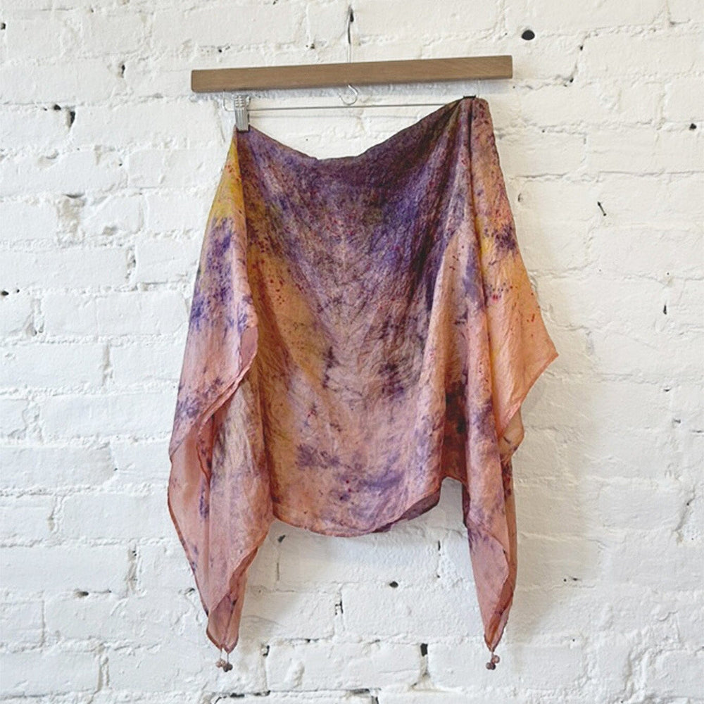 Colorful tie dye silk scarf hanging on a wooden rod against a white brick wall