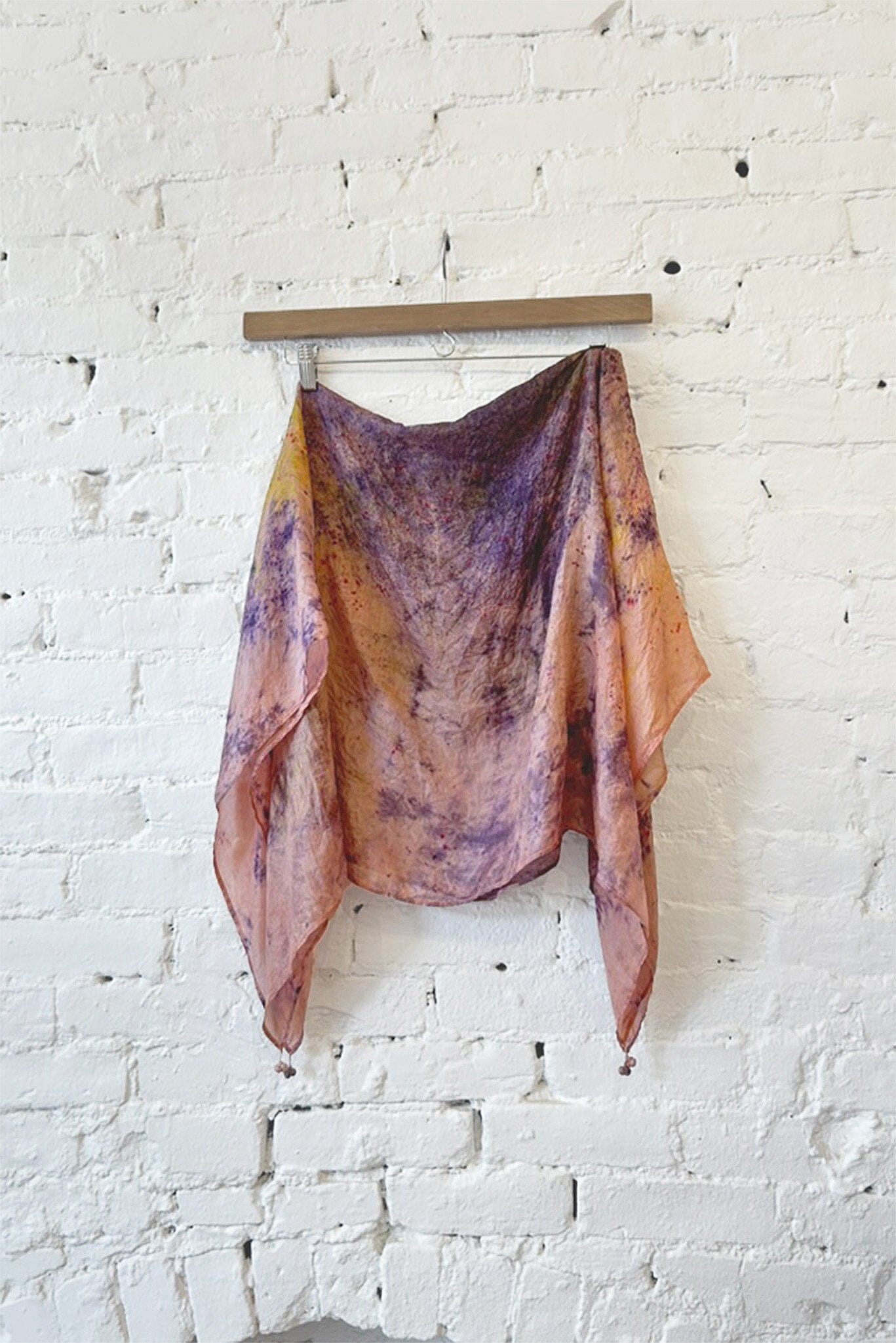 Colorful tie dye silk scarf hanging on a wooden rod against a white brick wall