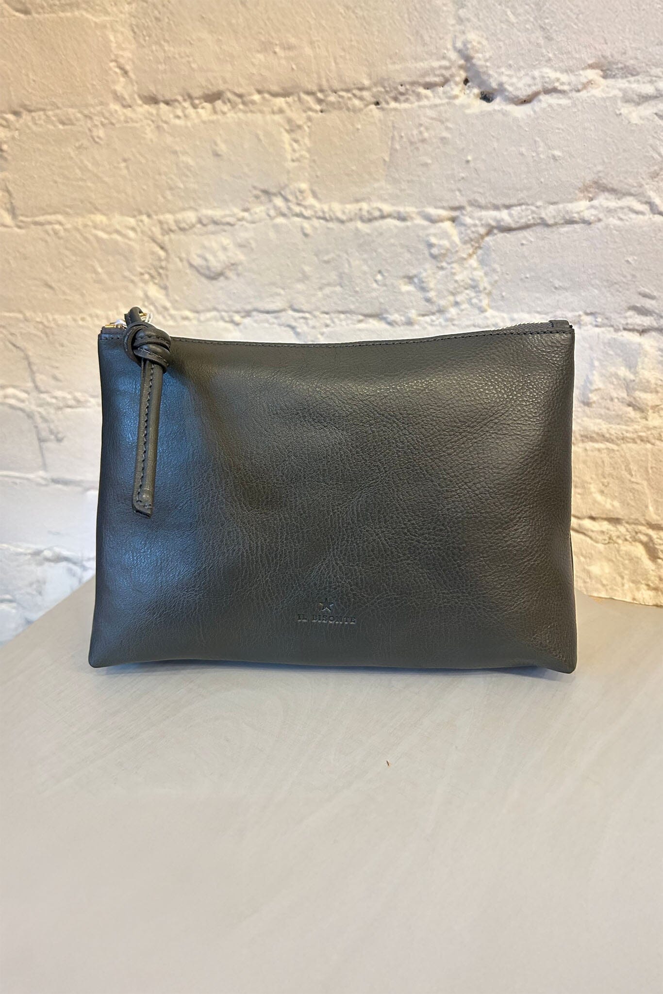 Black leather zipper pouch on a light gray surface with a textured white wall background