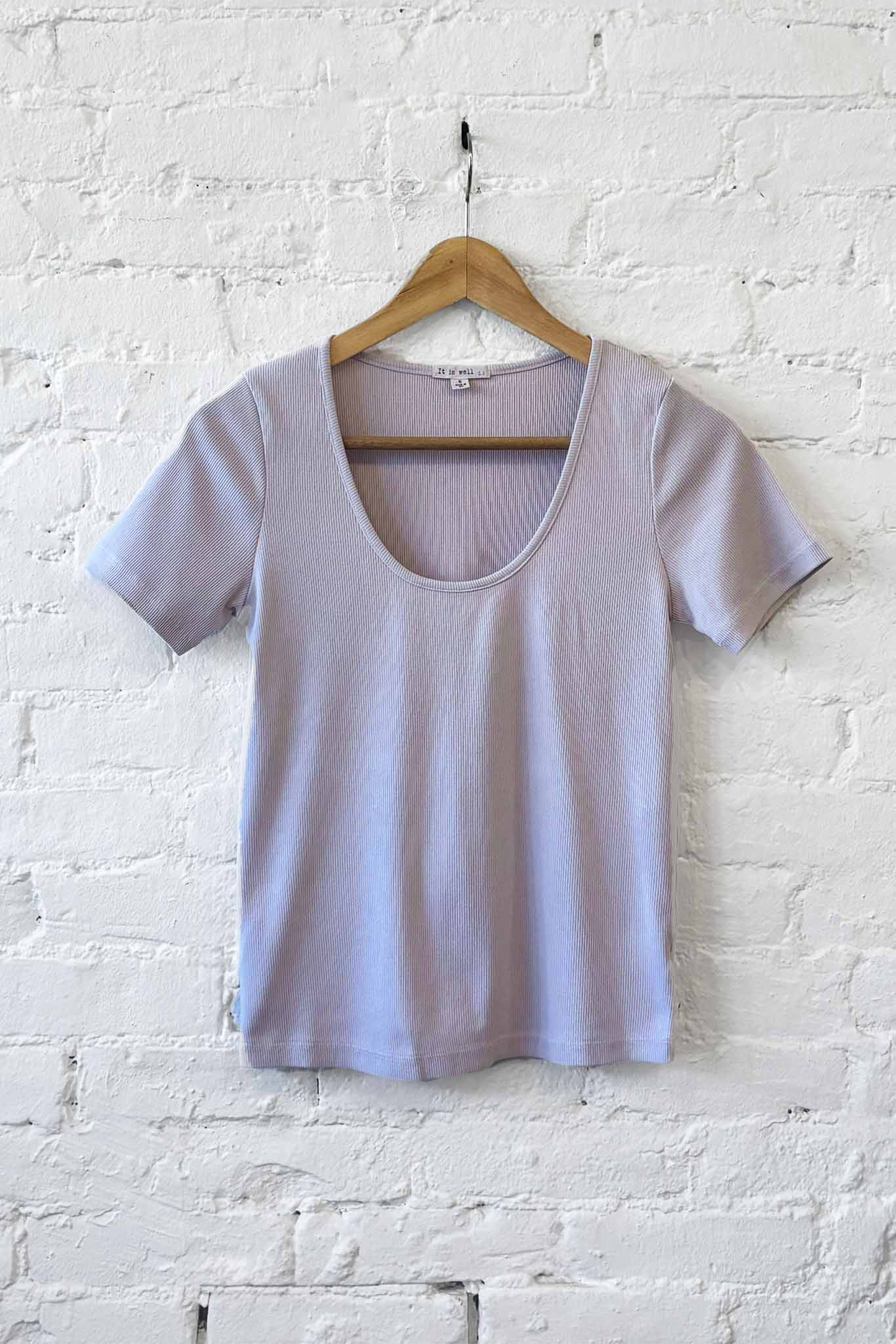Light purple t-shirt on a wooden hanger against a white brick wall.