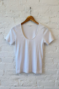 White t-shirt on a wooden hanger against a white brick wall