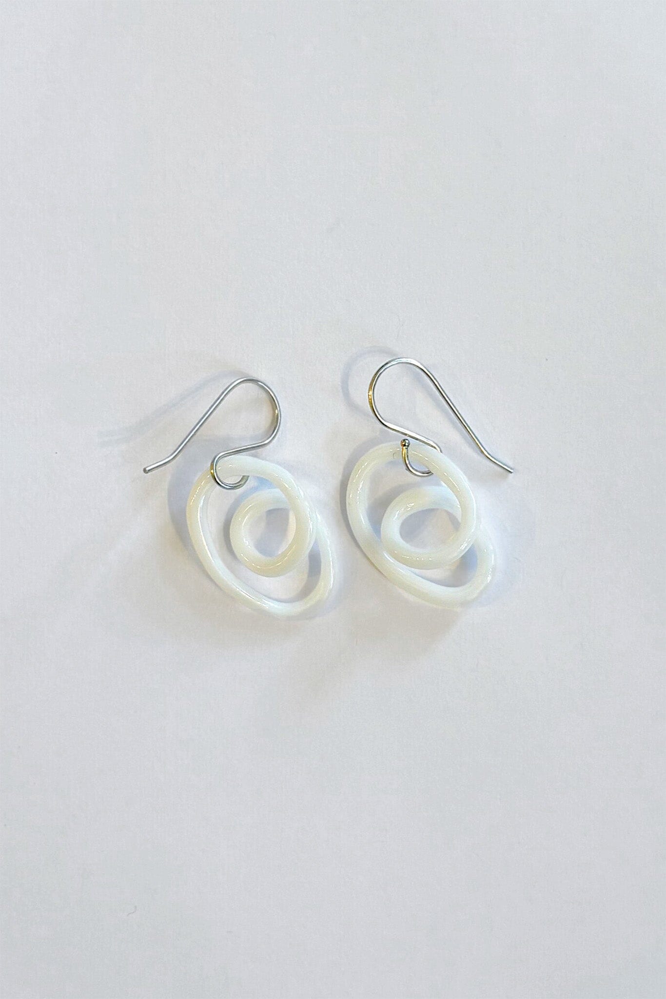 Pair of white glass spiral earrings on a light gray background