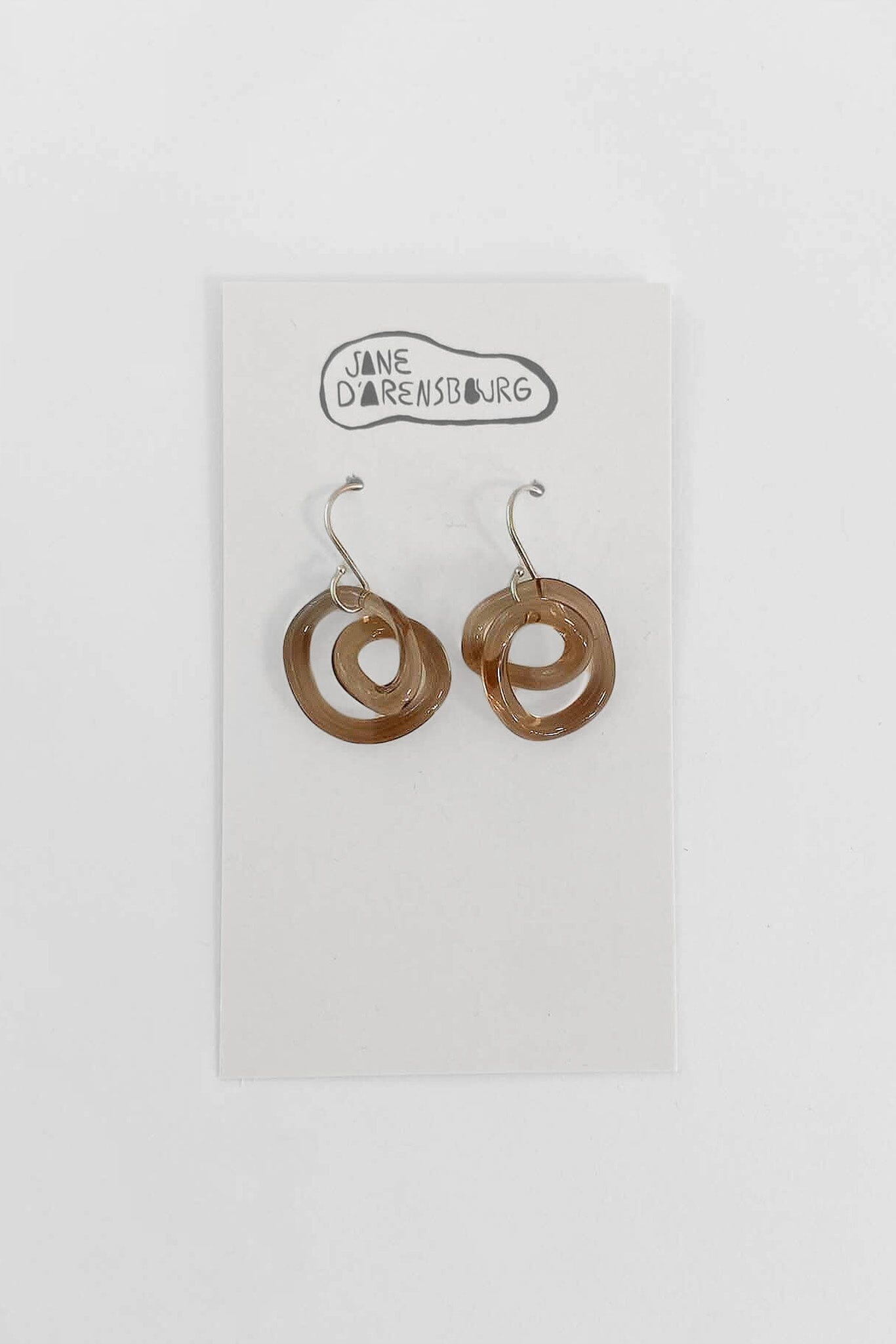 A pair of brown glass small squiggle earrings in mauve color with sterling silver earring wires, displayed on a white card with 'Jane D'Arensbourg' branding.