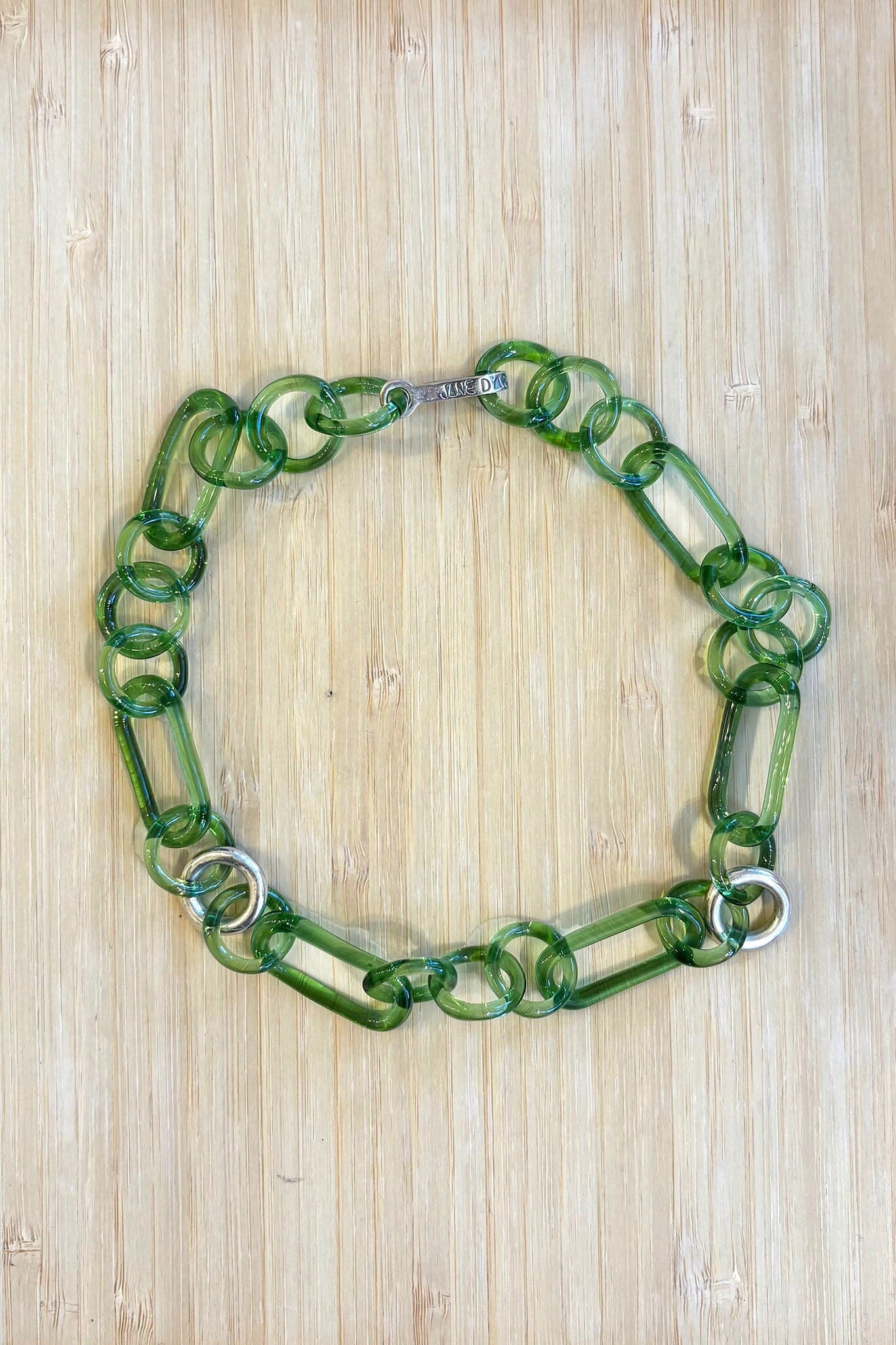 Green glass necklace with sterling silver accents on a wooden surface