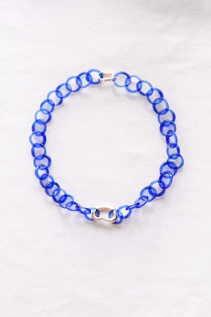 A silver and blue glass link necklace with a brass bean charm, displayed against a white background.