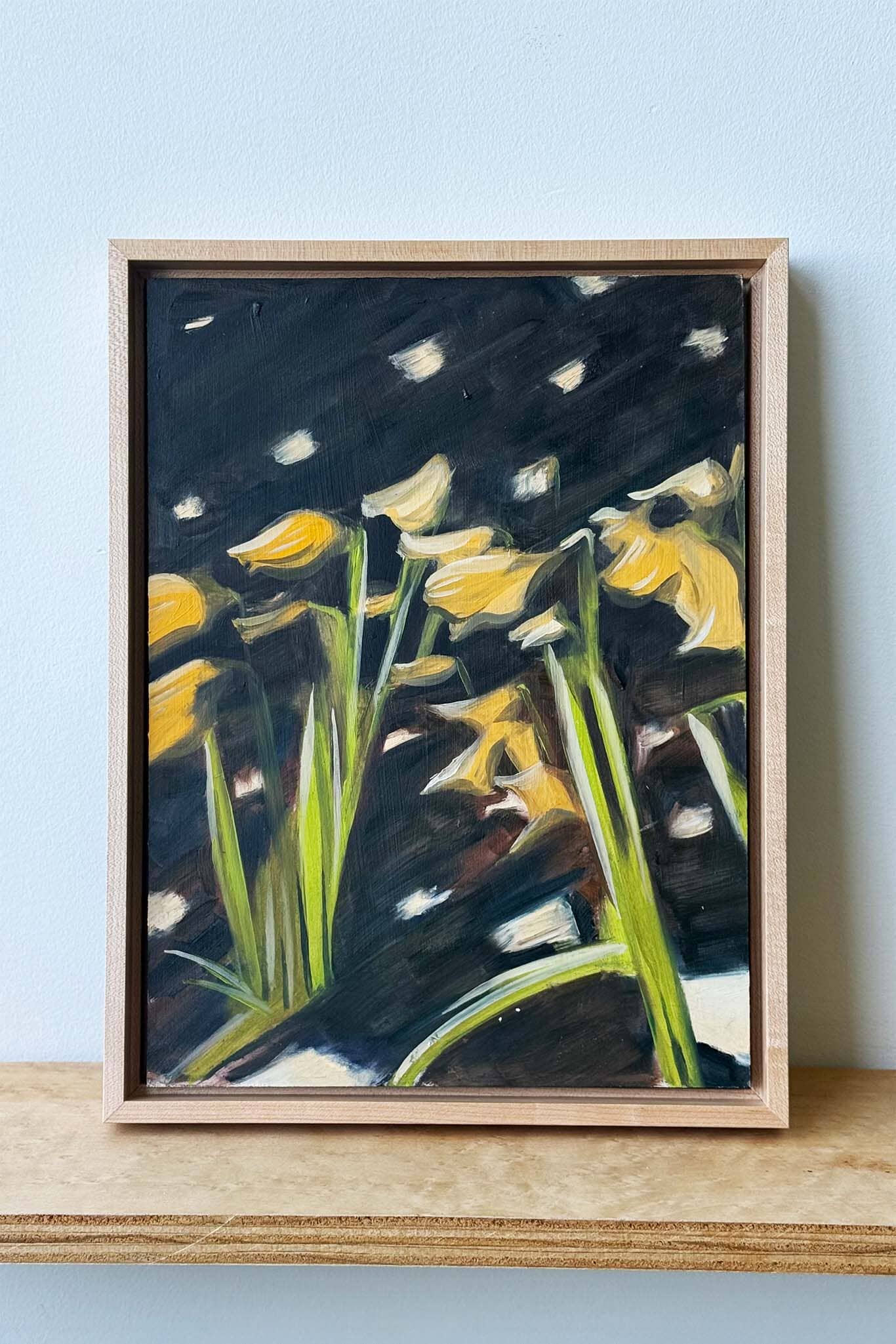 Framed artwork of yellow flowers against a dark background on a light blue wall.
