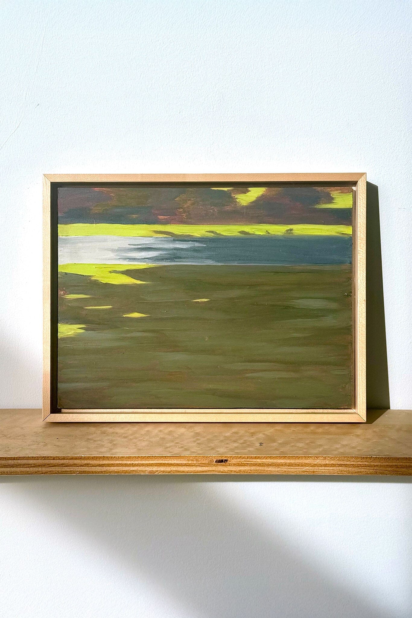 Framed abstract painting on a wooden shelf against a white wall