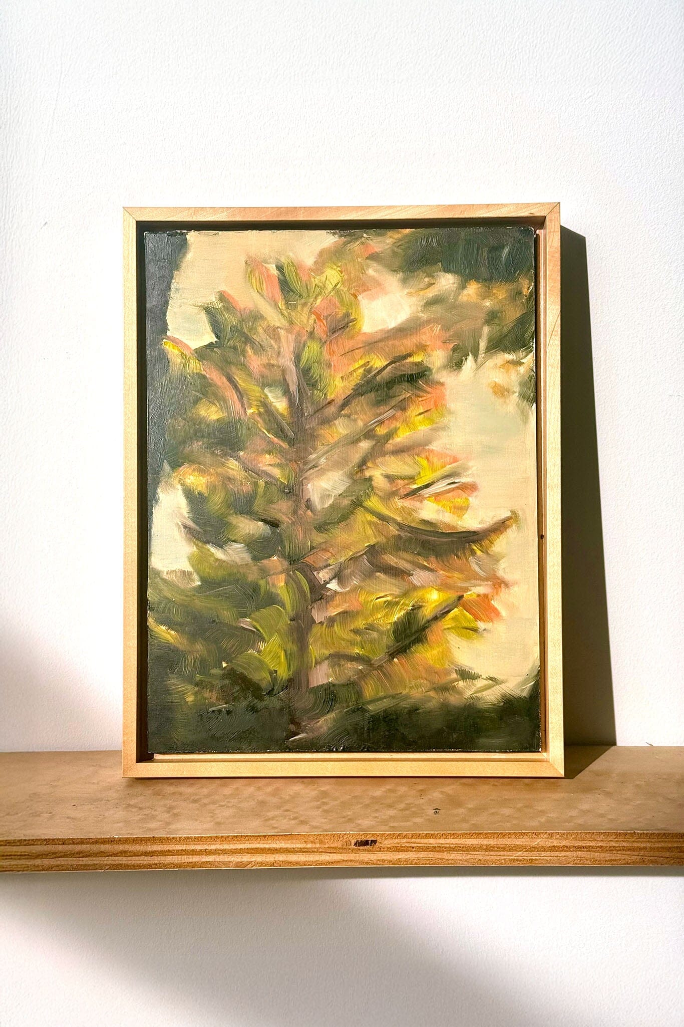 Framed painting of a tree on a wooden shelf with a white background