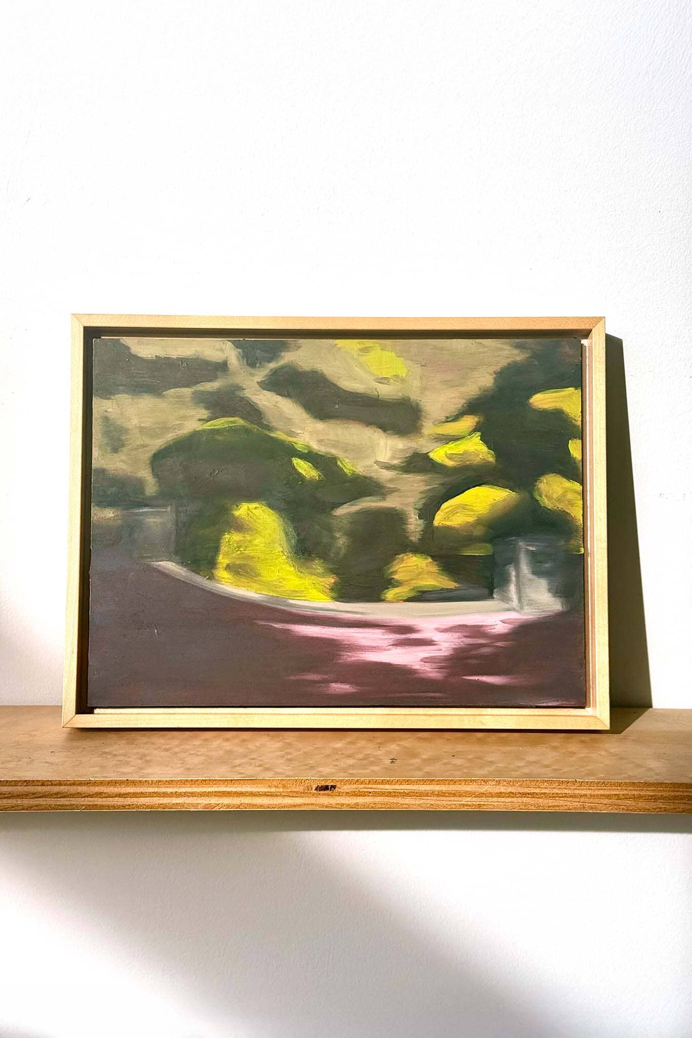 Framed abstract painting on a wooden shelf with a white background