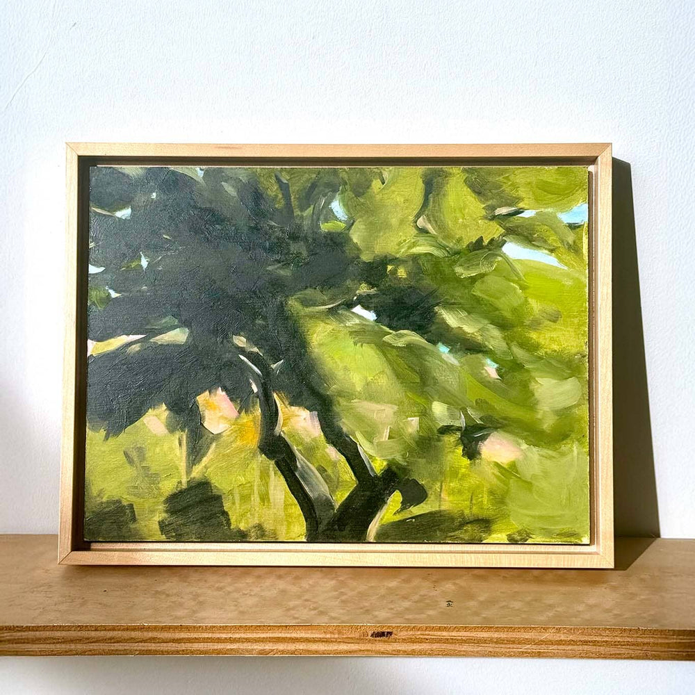 Framed painting of a green leafy scene on a wooden shelf with a white background