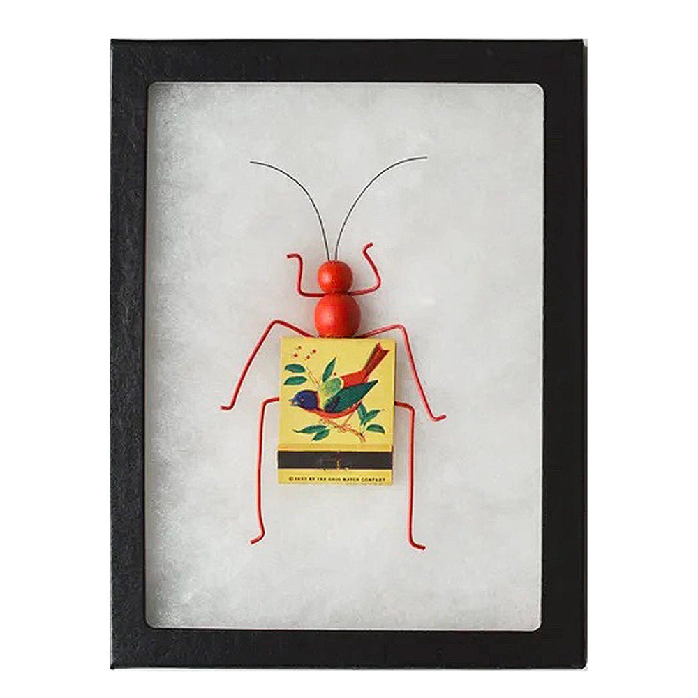 Framed artwork of a red insect-like figure with a yellow matchbook featuring a bird design on a white background.
