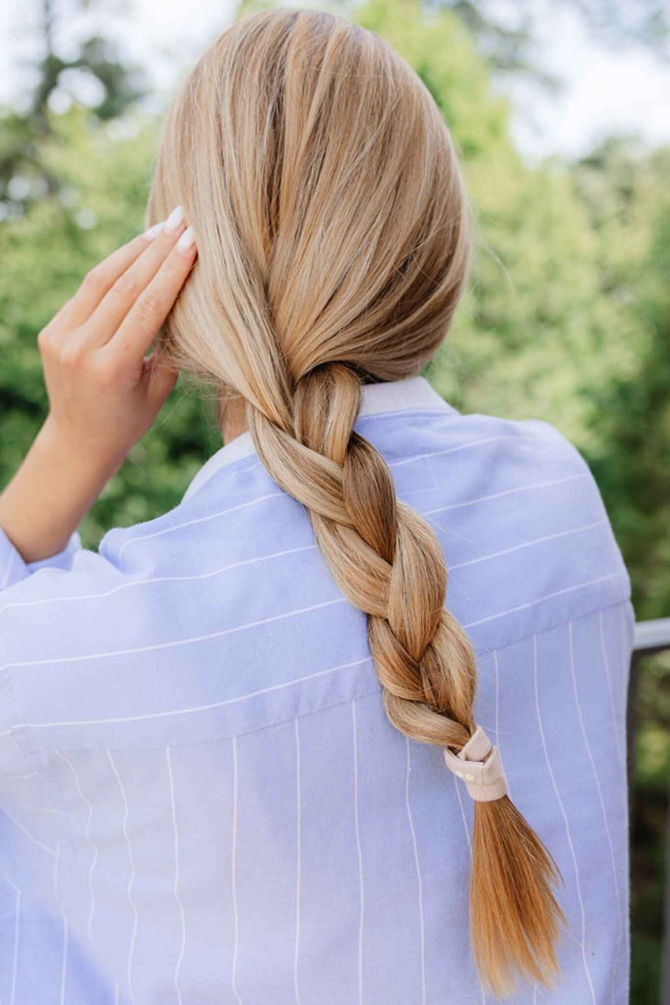 Person with a long braid wearing a light blue shirt outdoors.