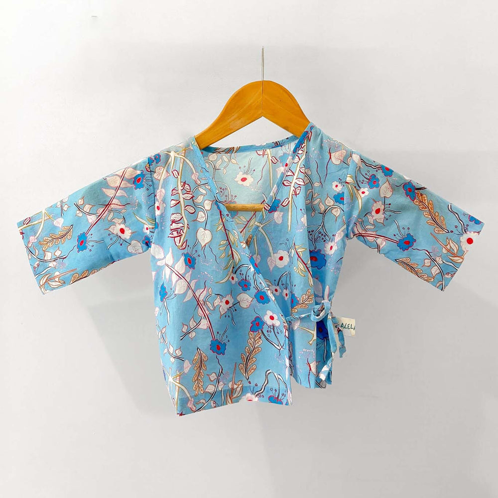Light blue kimono-style baby pajama top with floral patterns on a wooden hanger against a white background