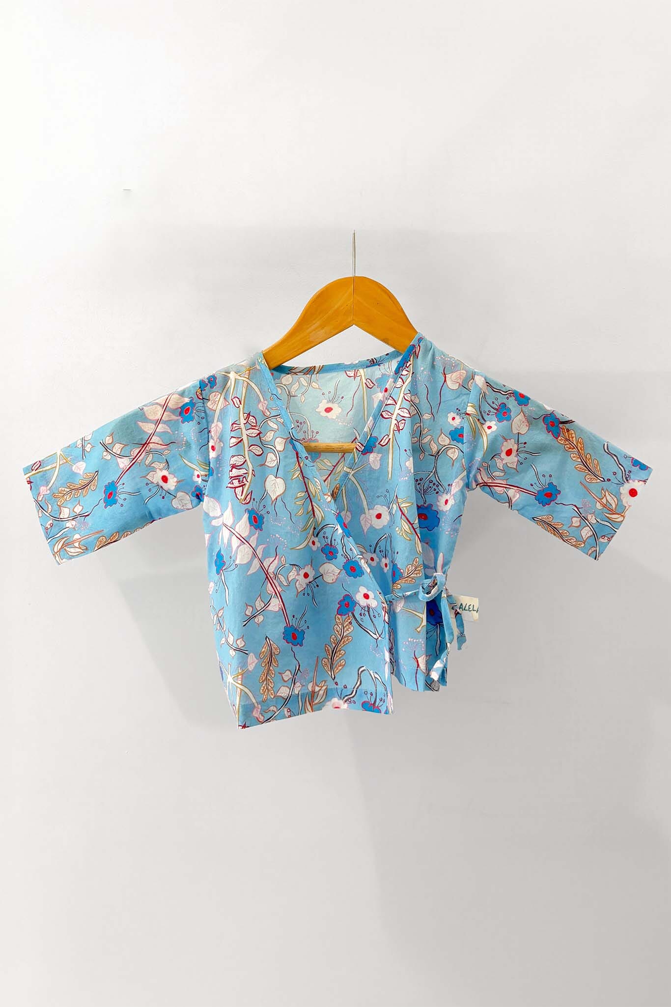 Light blue kimono-style baby pajama top with floral patterns on a wooden hanger against a white background