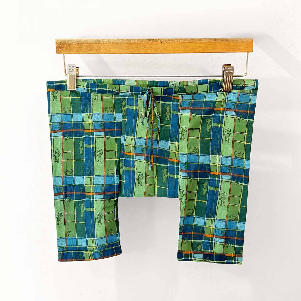 Green and blue checkered pajama bottoms on a wooden hanger against a white background