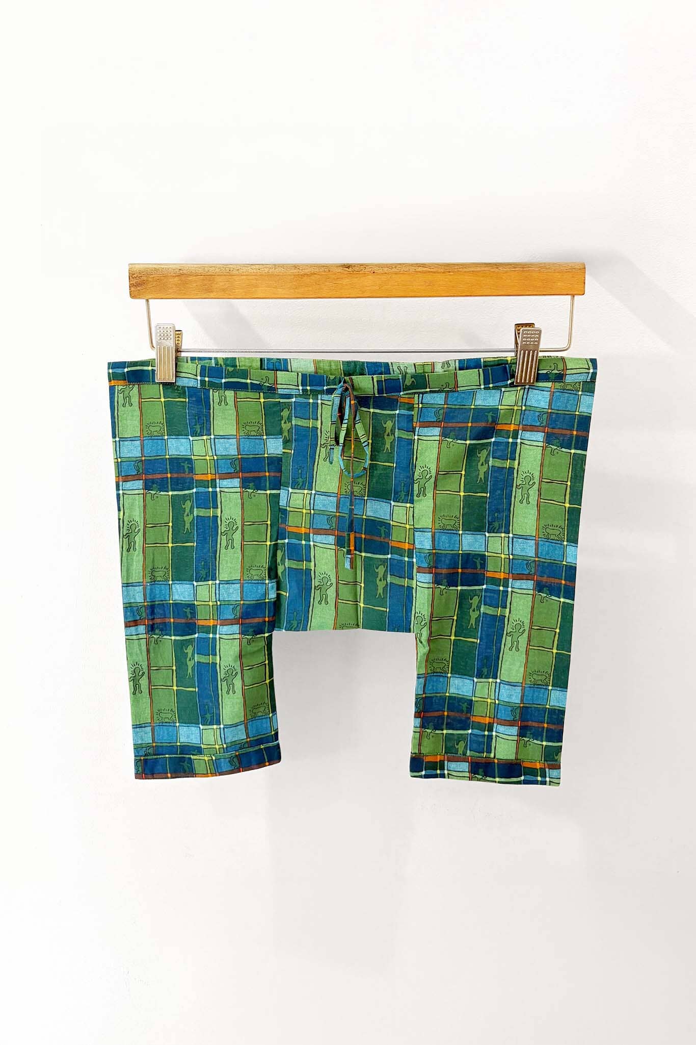 Green and blue checkered pajama bottoms on a wooden hanger against a white background