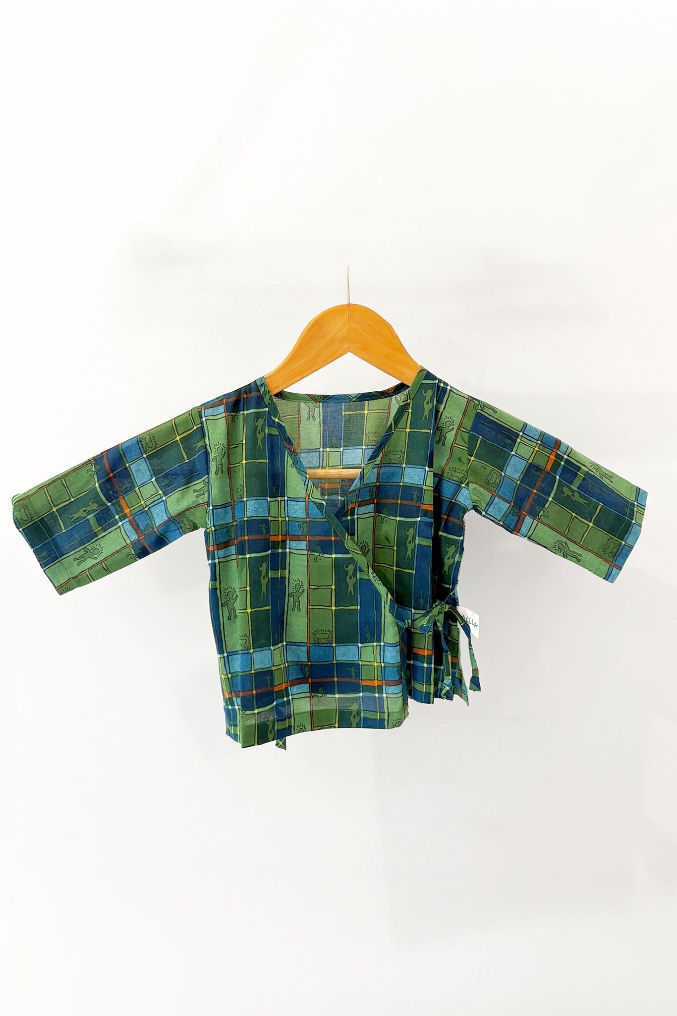 Green and blue checkered baby pajama top on a wooden hanger against a white background
