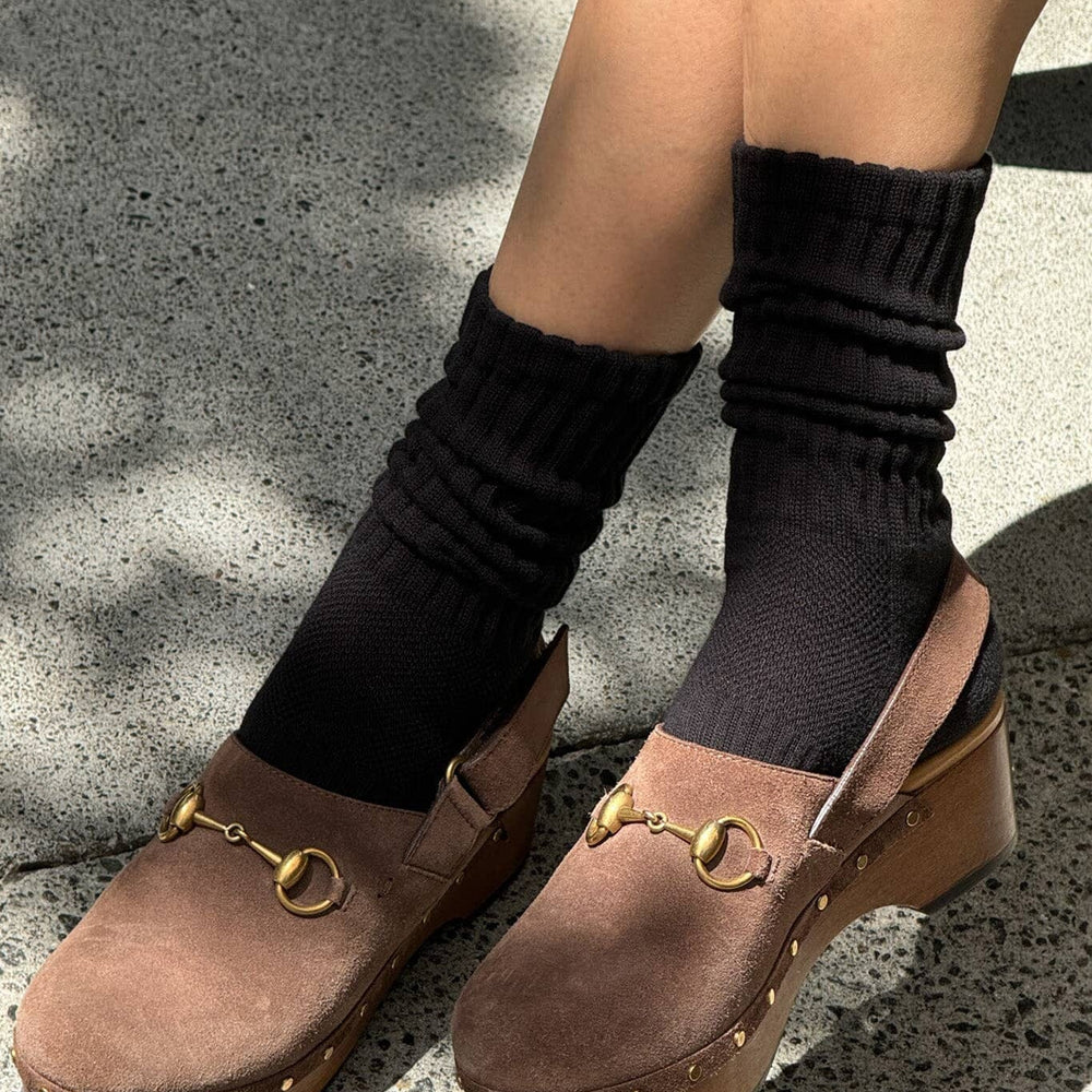 Brown clogs with gold details worn with black socks on a concrete surface