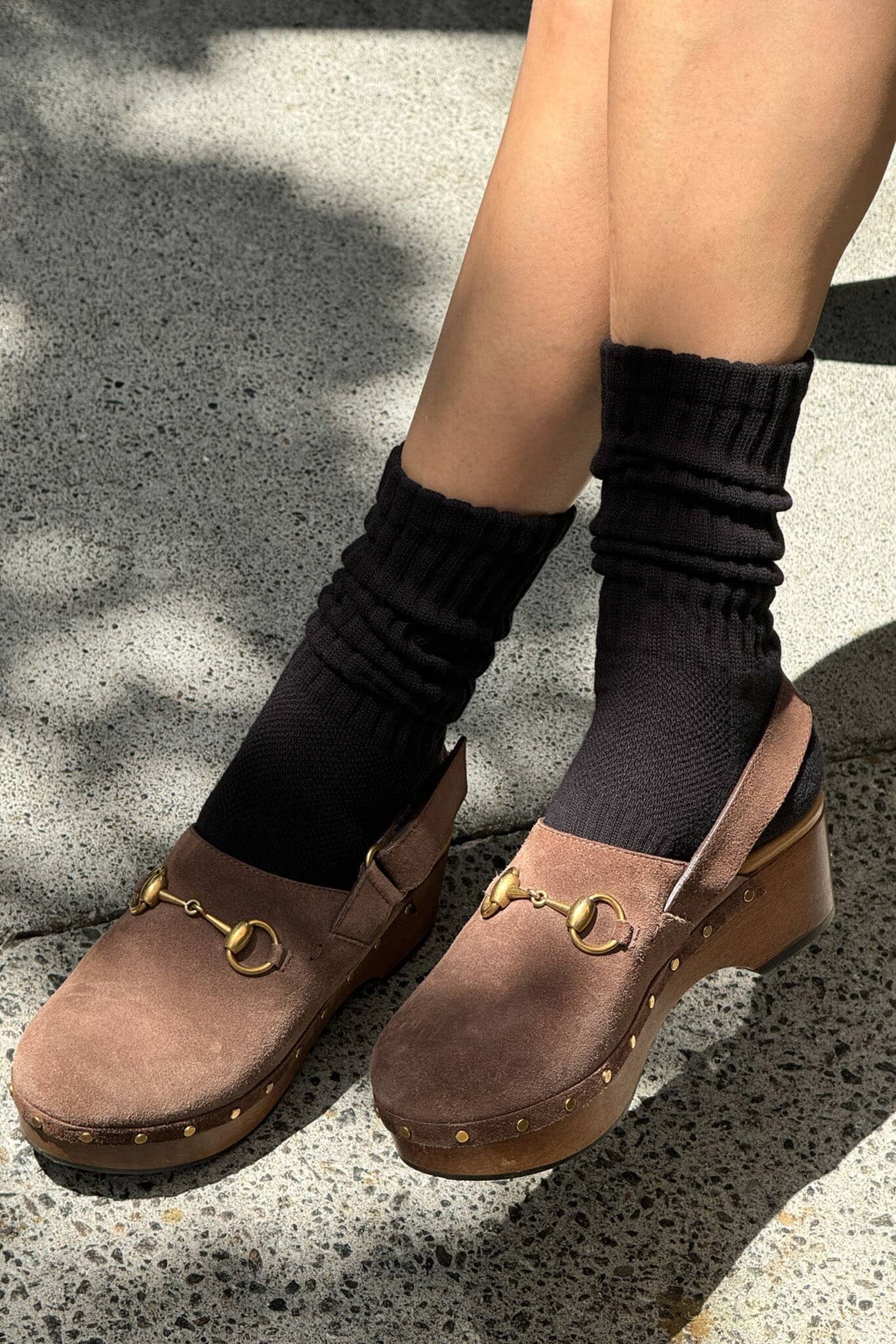 Brown clogs with gold details worn with black socks on a concrete surface