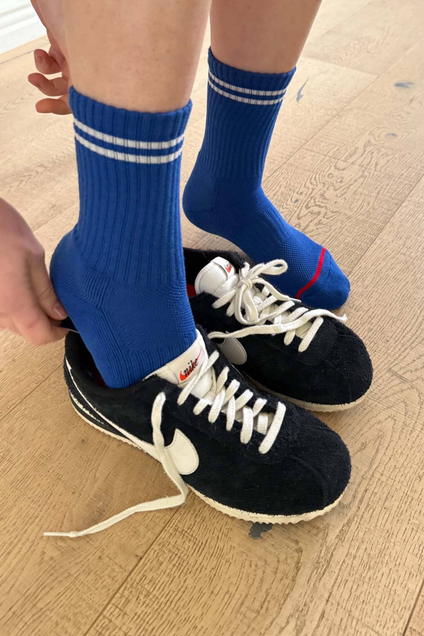 Person wearing blue socks with white stripes and black sneakers on a wooden floor.