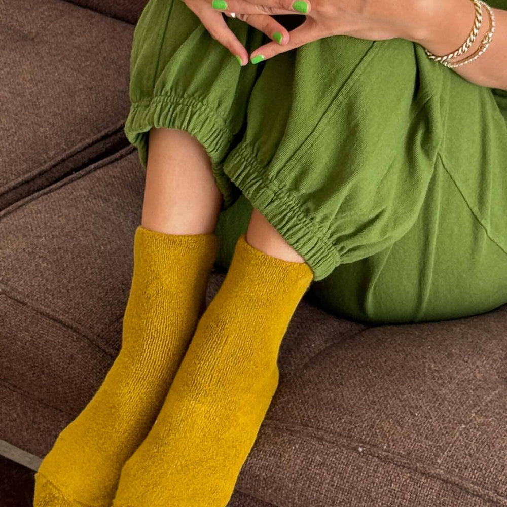 Person wearing green pants and mustard yellow socks sitting on a brown couch.