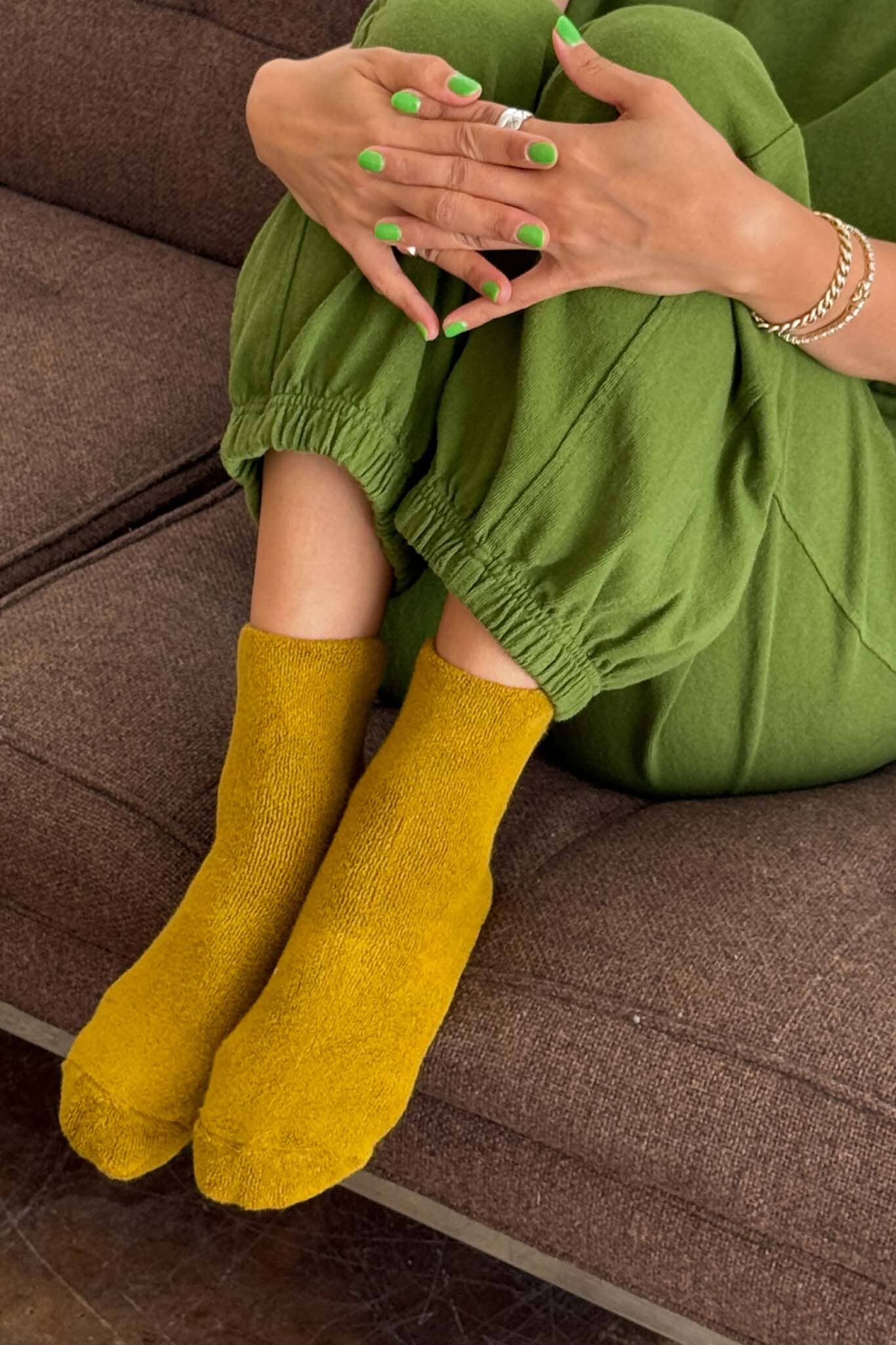 Person wearing green pants and mustard yellow socks sitting on a brown couch.