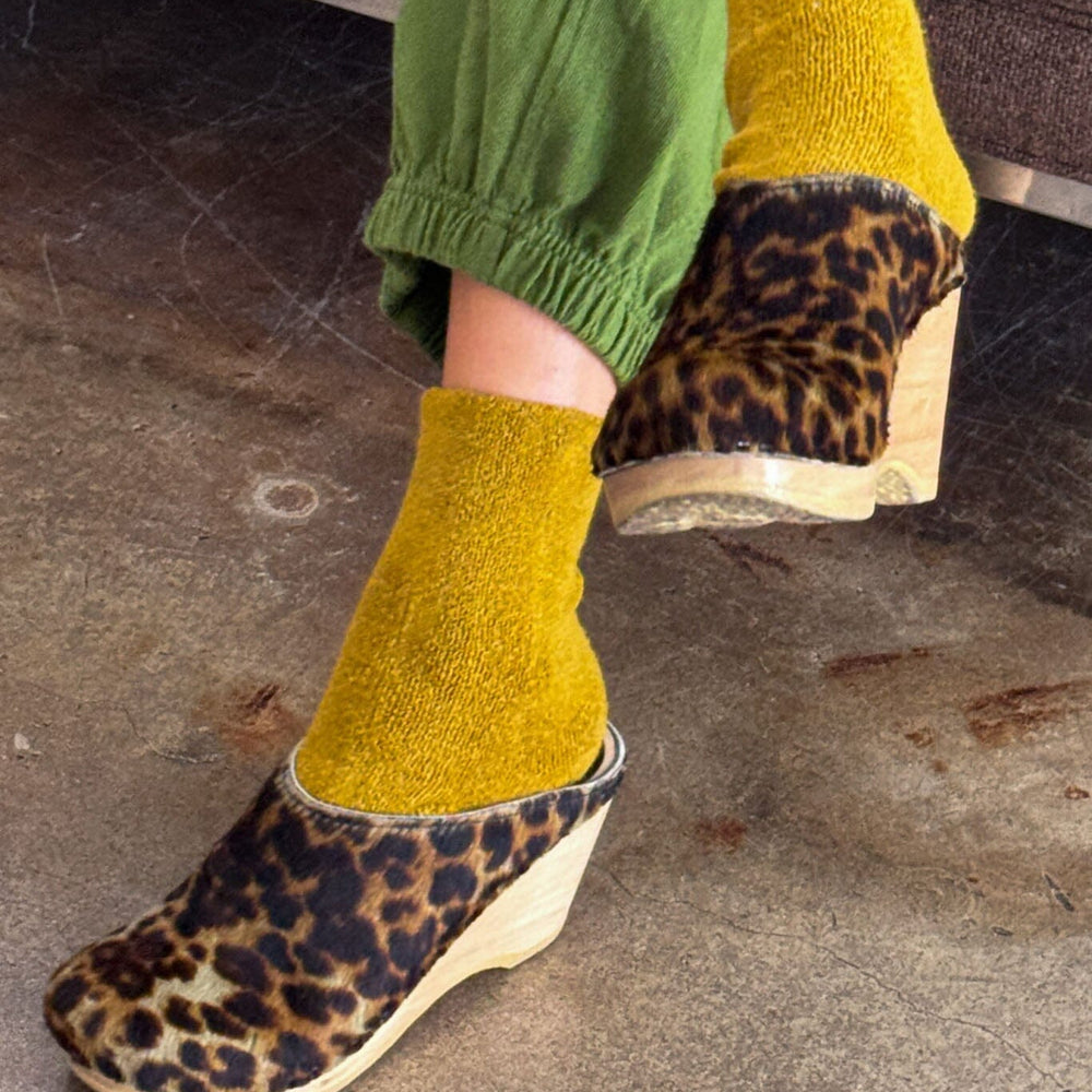 
                  
                    Person wearing mustard yellow socks and leopard print shoes on a concrete floor.
                  
                