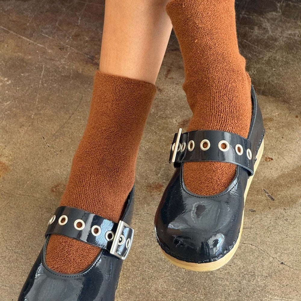 Black shoes with buckle details worn with brown socks on a concrete floor.