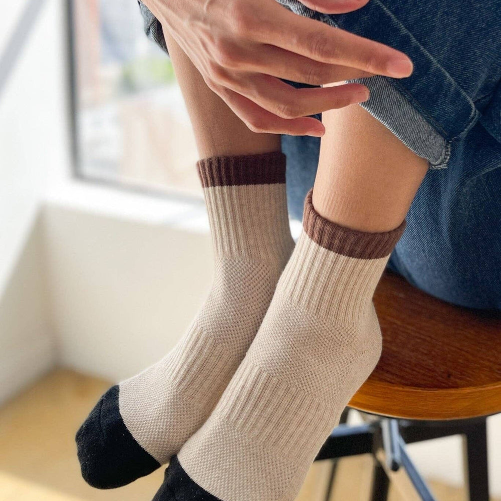 Person wearing beige socks with brown accents sitting on a chair indoors.