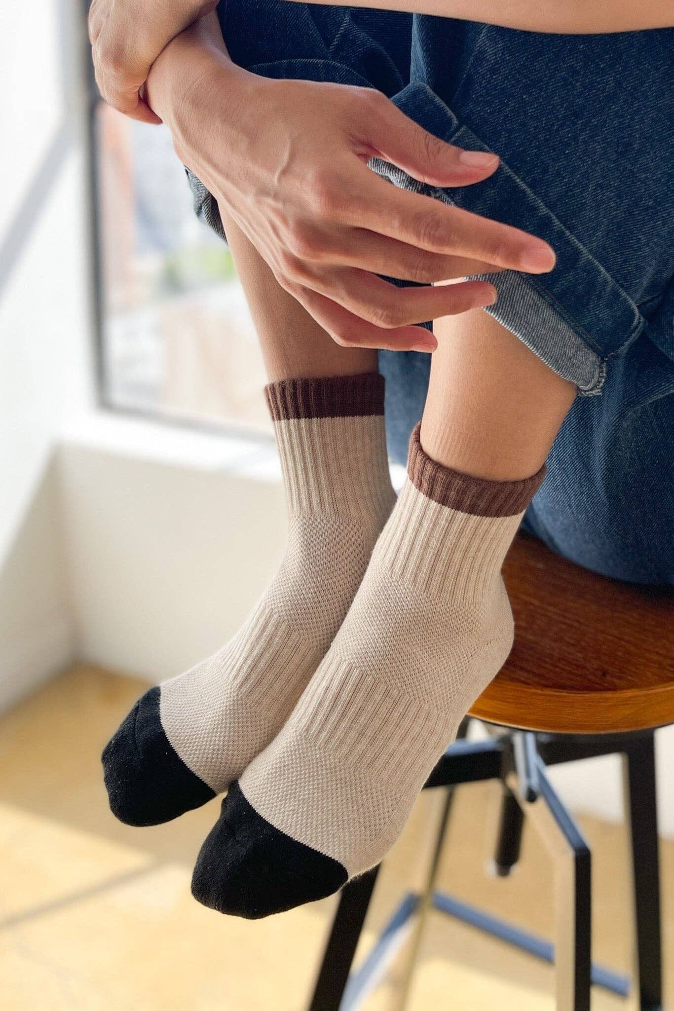 Person wearing beige socks with brown accents sitting on a chair indoors.