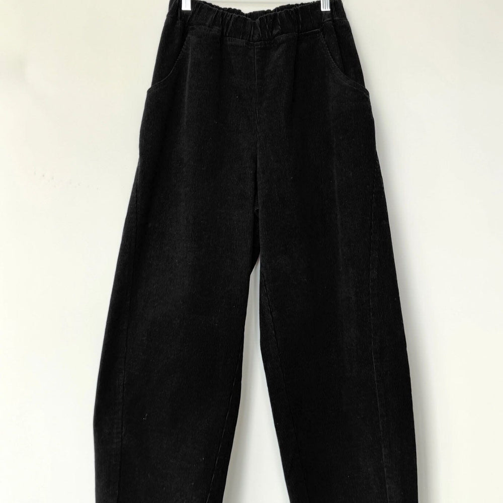 Black corduroy pants hanging on a wooden hanger against a white background