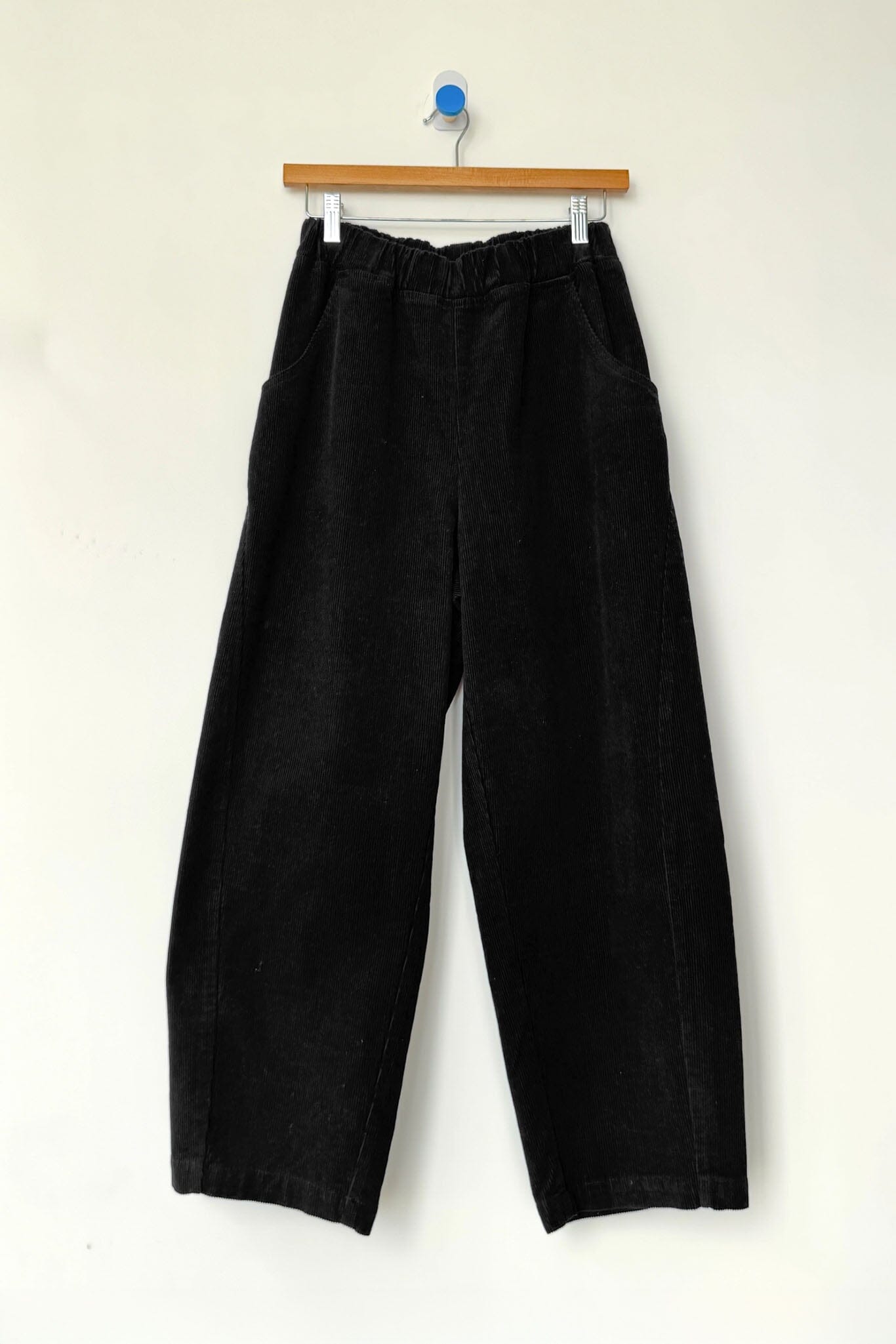 Black corduroy pants hanging on a wooden hanger against a white background