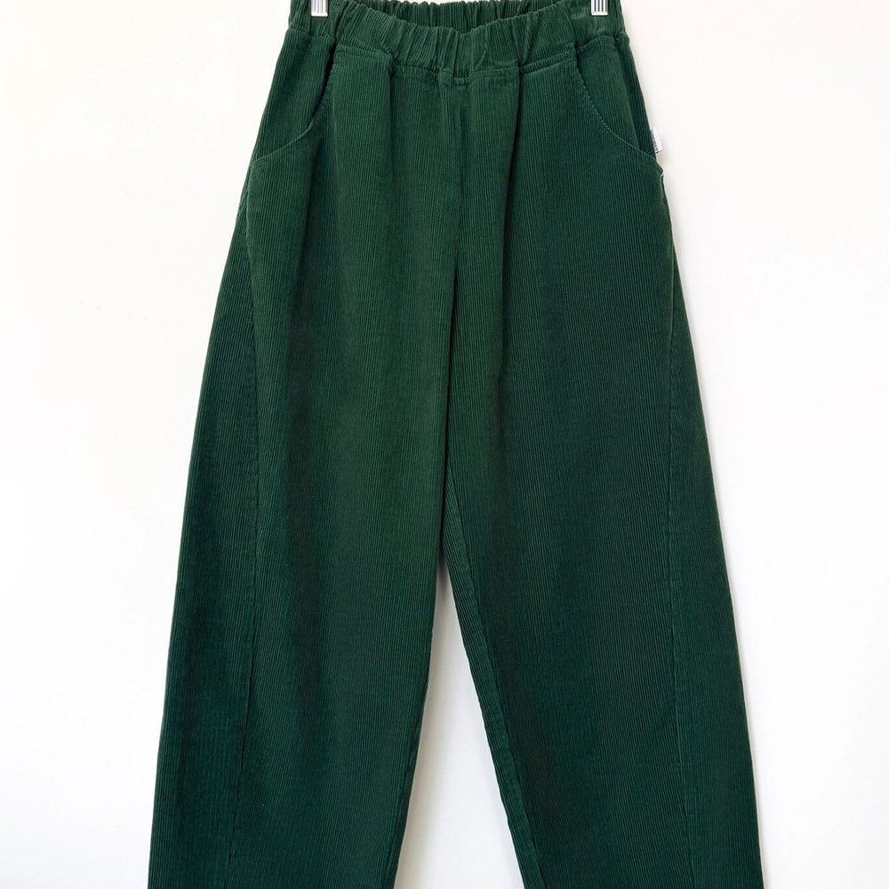 Green corduroy pants hanging on a wooden hanger against a white background