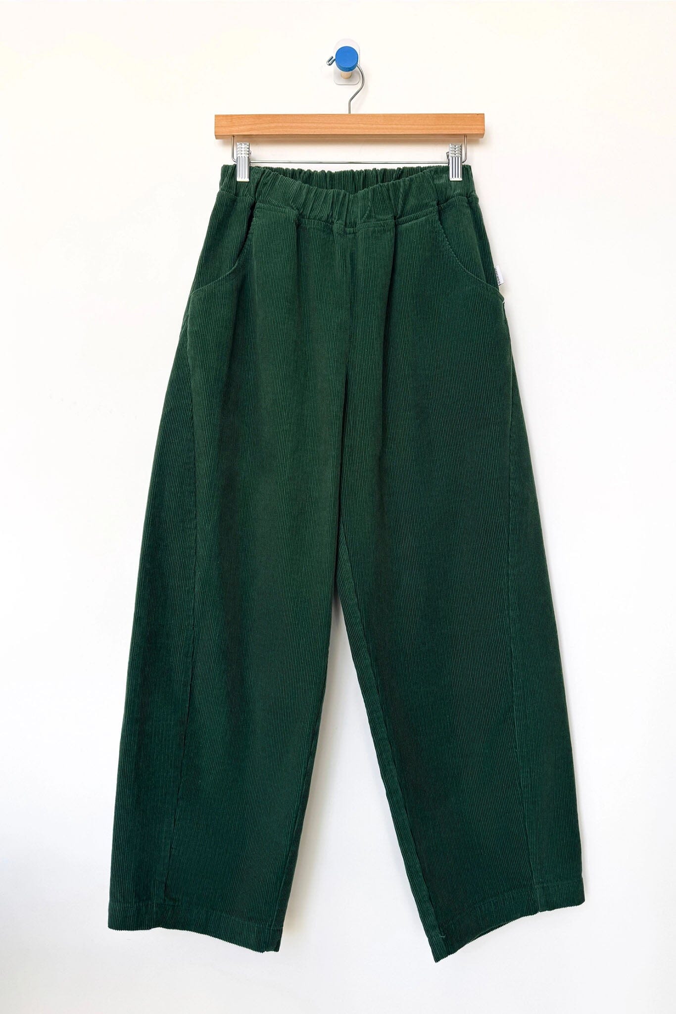 Green corduroy pants hanging on a wooden hanger against a white background