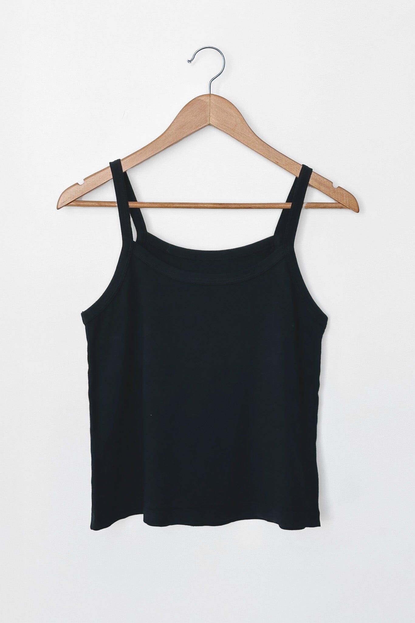 Black tank top on a wooden hanger against a white background