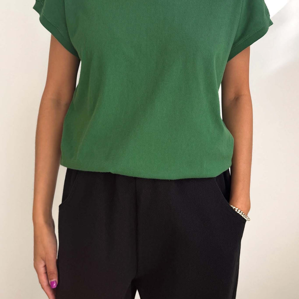 Person wearing a green t-shirt and black pants against a white background