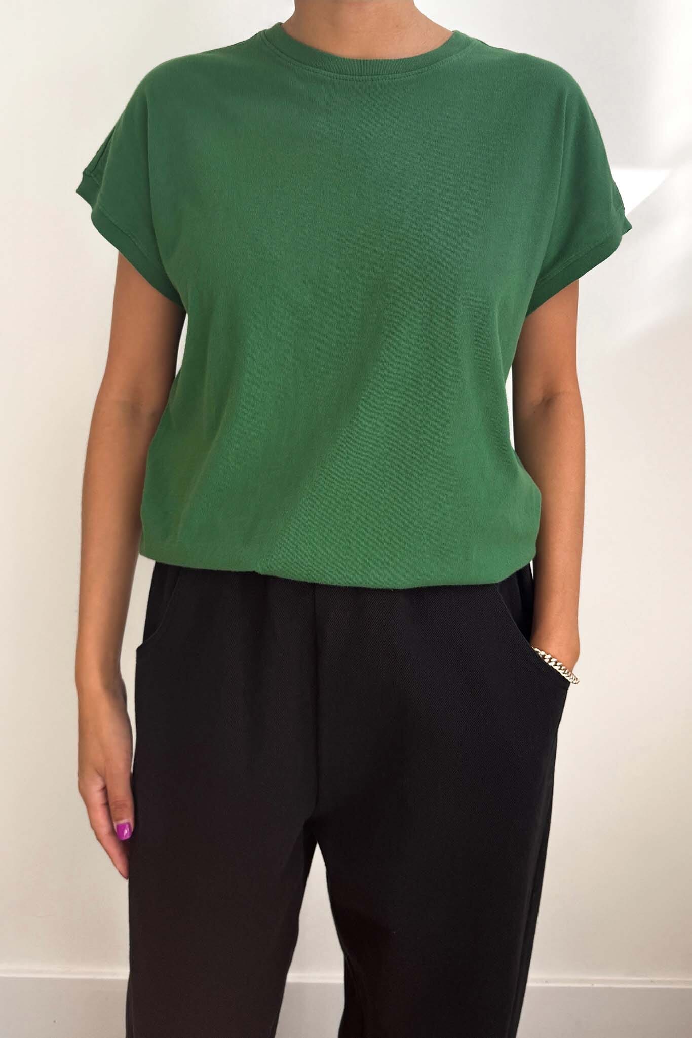 Person wearing a green t-shirt and black pants against a white background