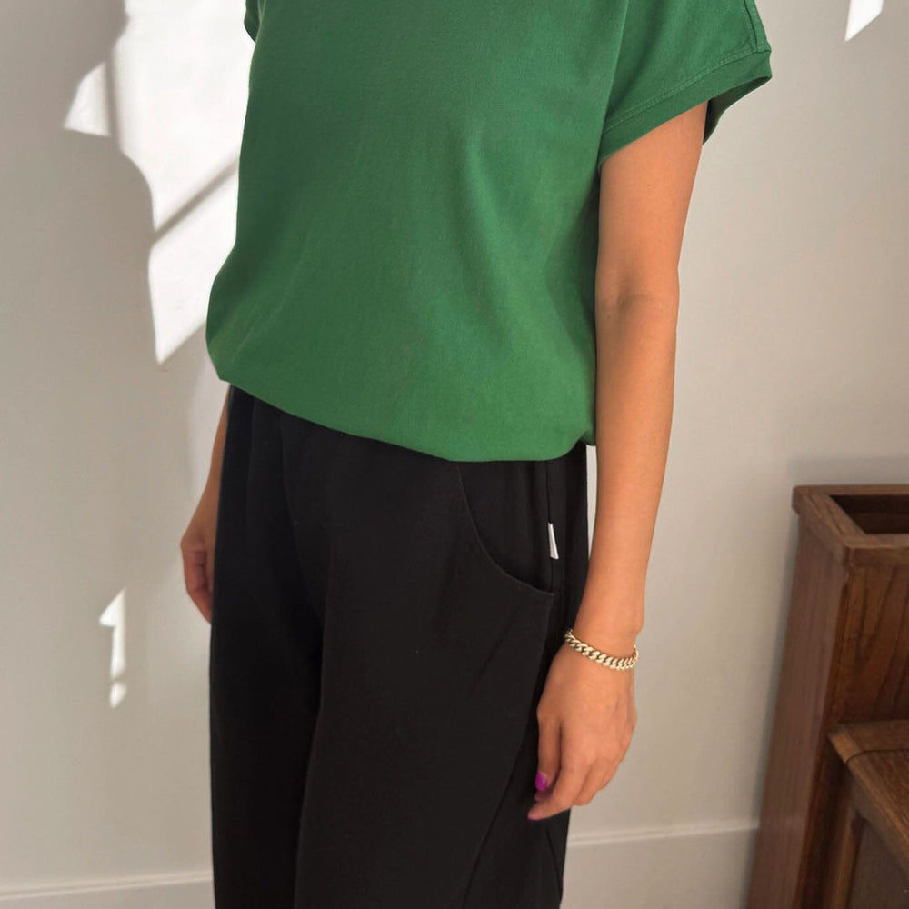 
                  
                    Person wearing a green t-shirt and black pants in a minimal indoor setting
                  
                