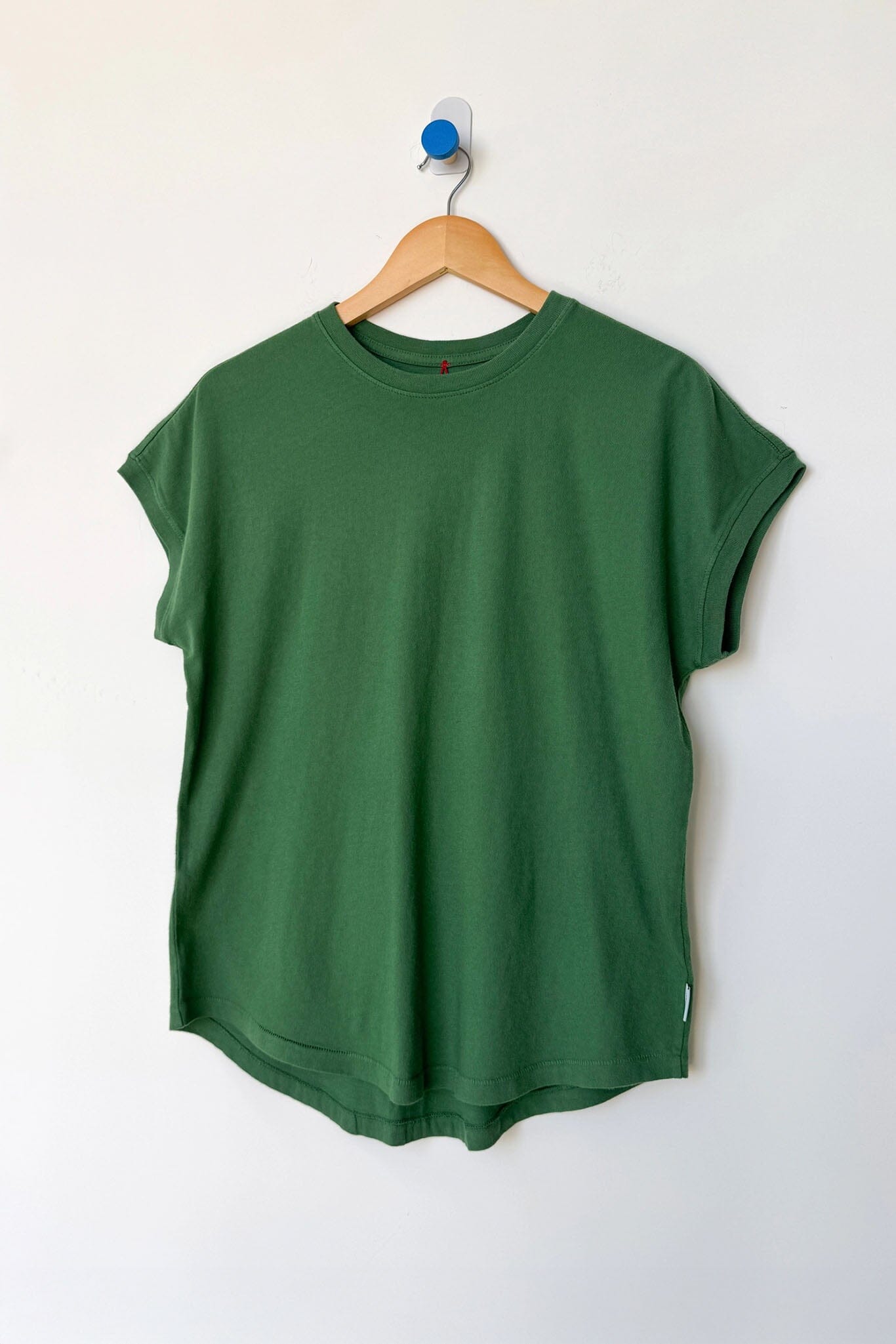 Green t-shirt on a wooden hanger against a white wall