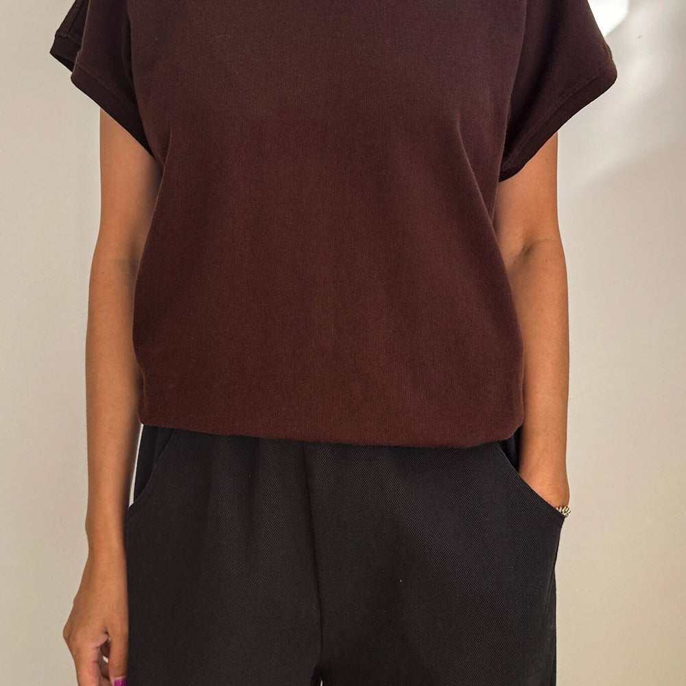 Person wearing a brown t-shirt and black pants against a neutral background