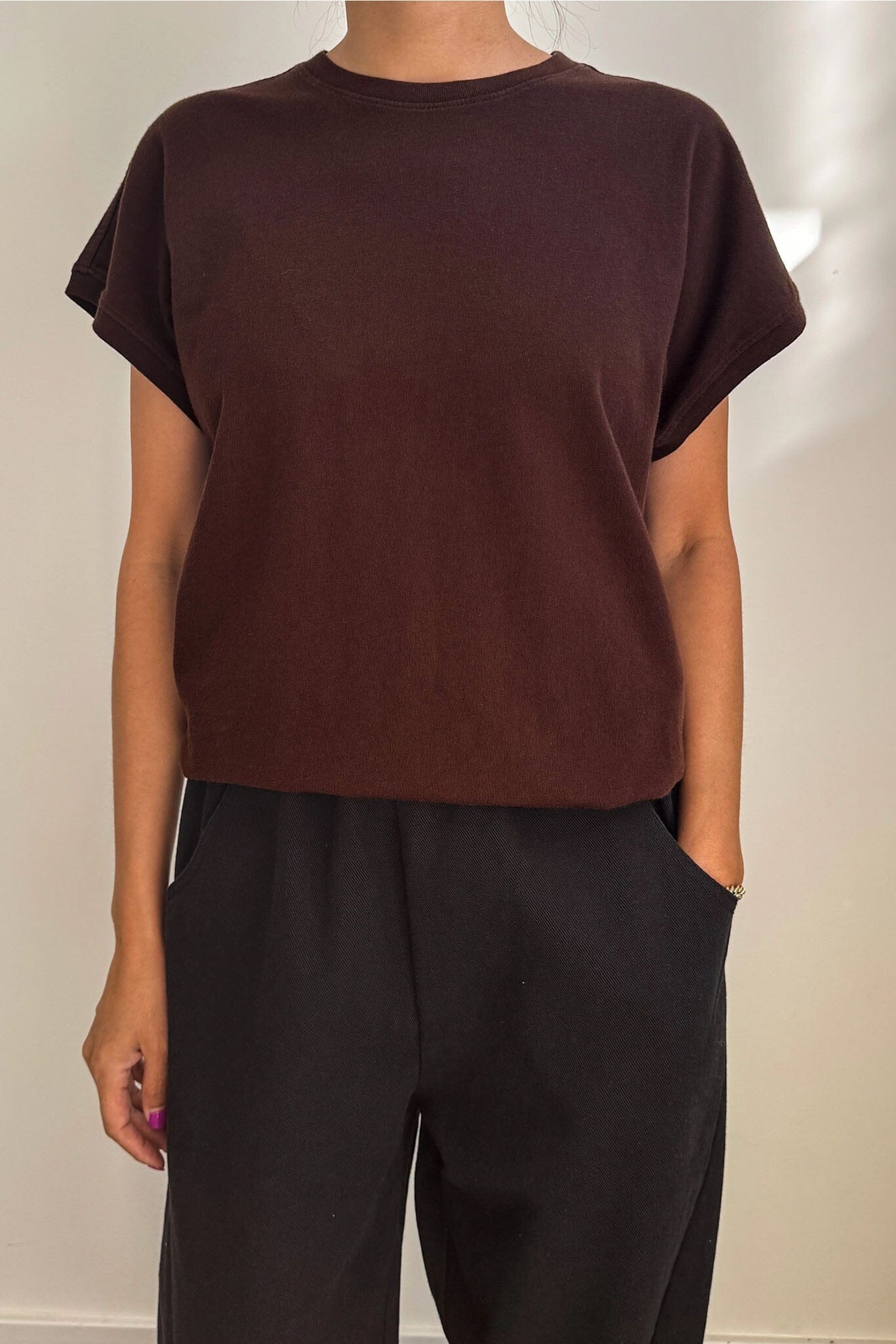 Person wearing a brown t-shirt and black pants against a neutral background