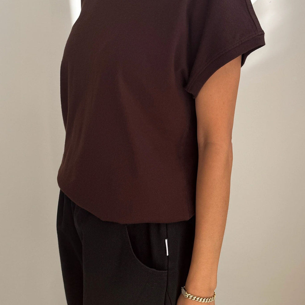 
                  
                    Person wearing a brown t-shirt and black pants against a plain background
                  
                