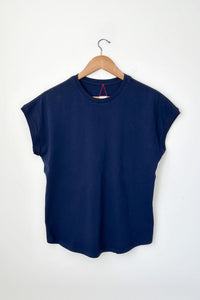 A navy blue short-sleeve crewneck t-shirt hanging on a wooden hanger against a plain white wall.