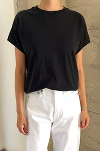 Person wearing a black t-shirt and white pants against a concrete wall.