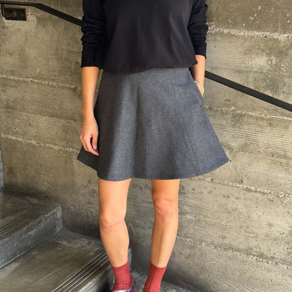 
                  
                    Person wearing a black top and gray skirt standing on concrete steps.
                  
                