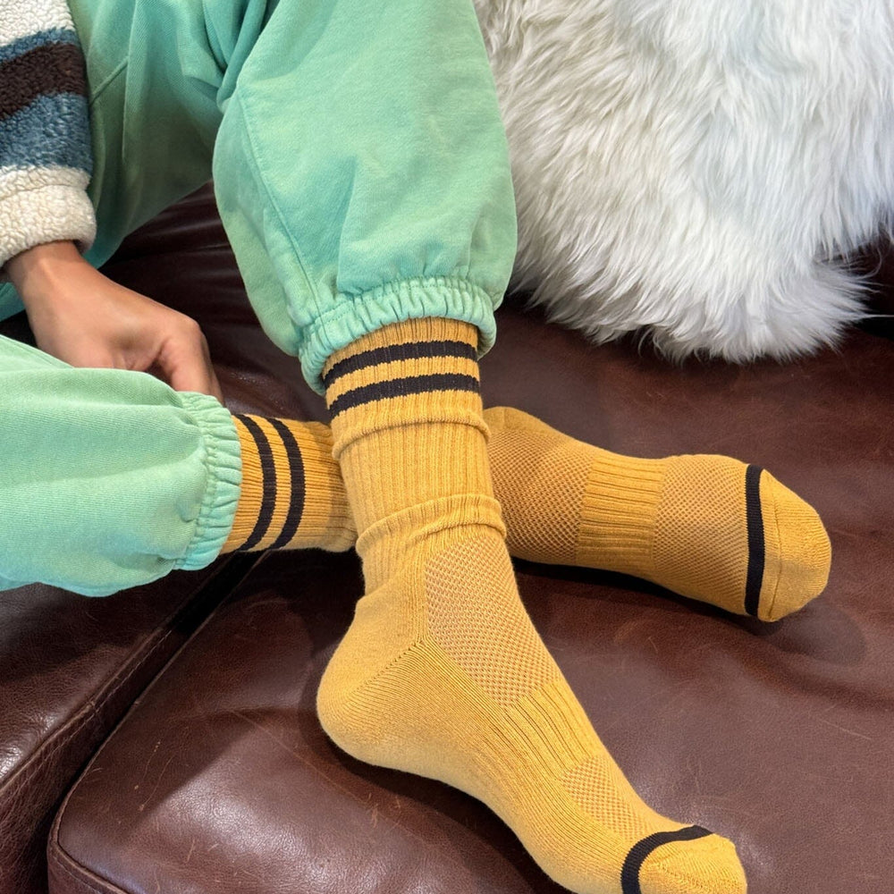 Person wearing yellow socks with black stripes on a brown couch.